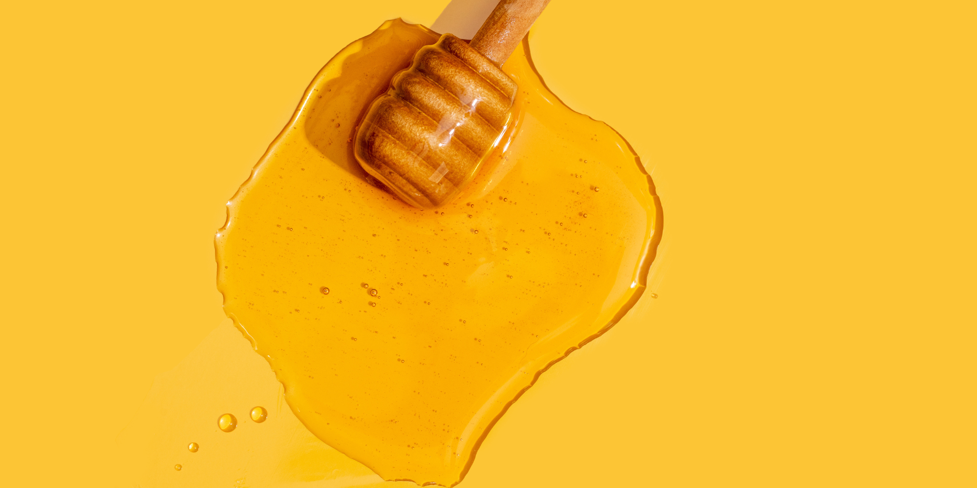 Honey stirrer full of honey lays on a yellow background. All around the stirrer is a blob of honey.