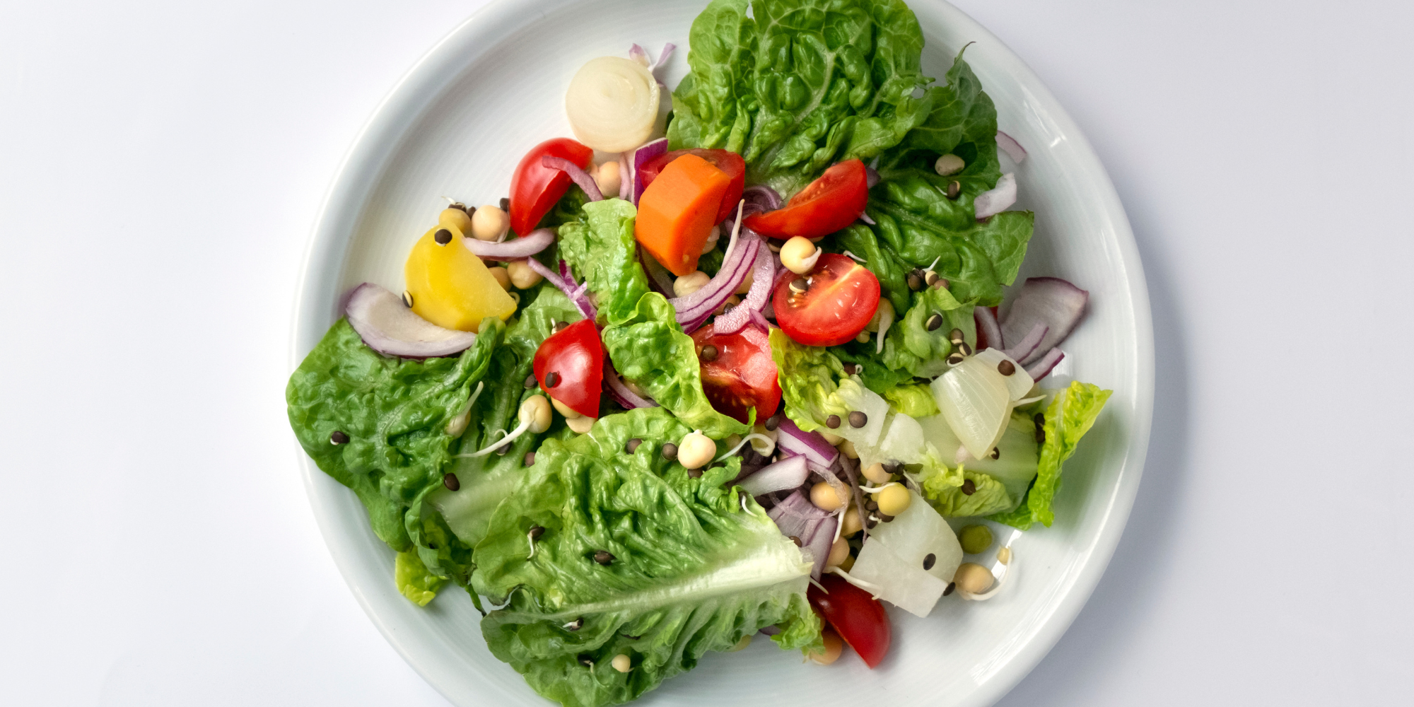White plate with raised edges against a white background. On the plate are a variety of leafy greens, grains, other vegetables and some cut strawberries